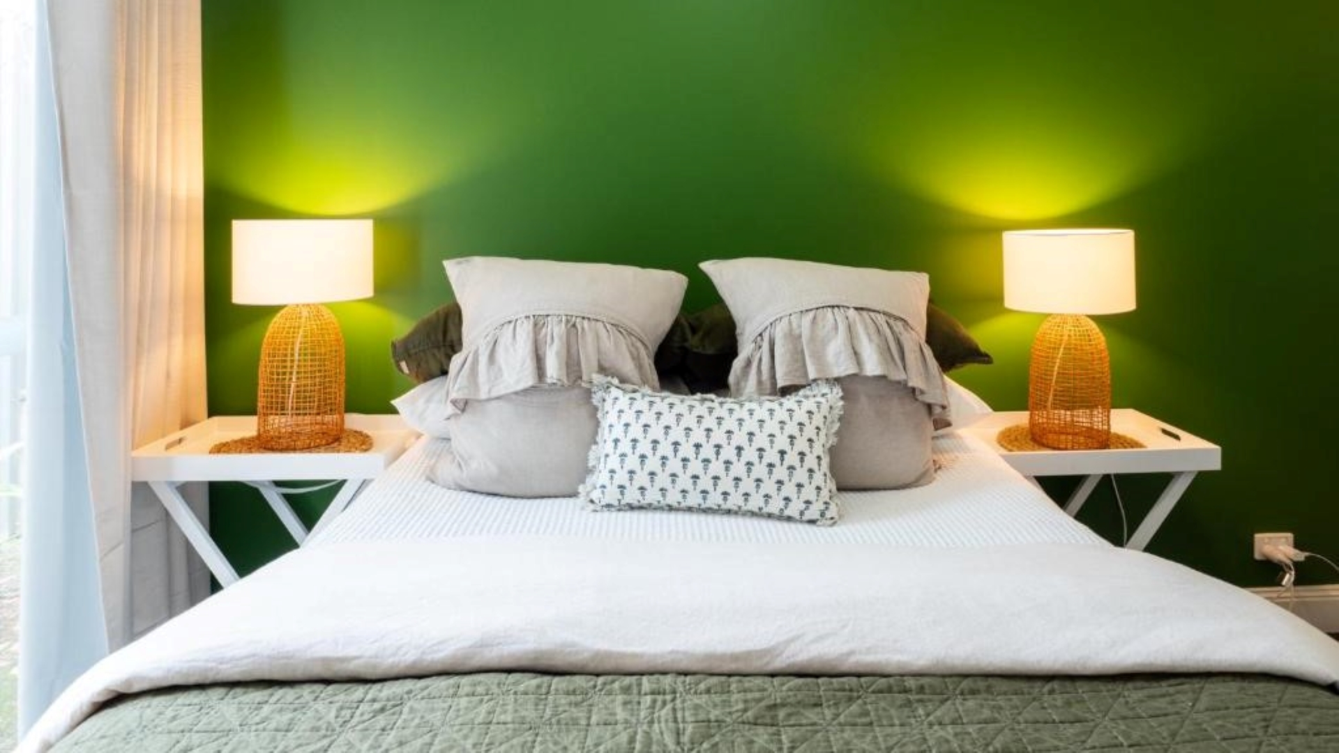 Image is of a queen sized bed with scatter cushions and green feature wall behind